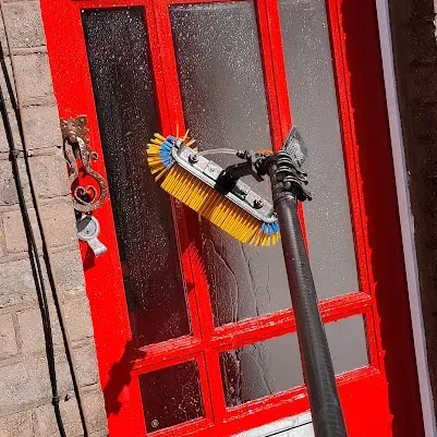 Water fed pole brush cleaning a red front door and its glass panels
